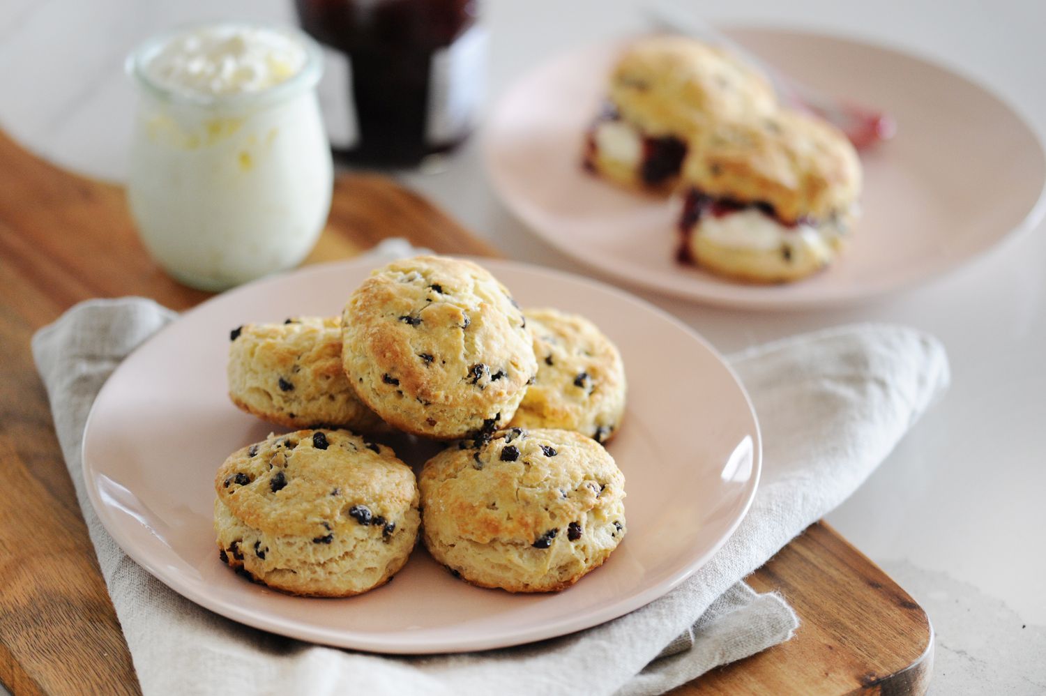 The BEST Irish Scones stacked on a plate with a second plate of scones and toppings behind it.