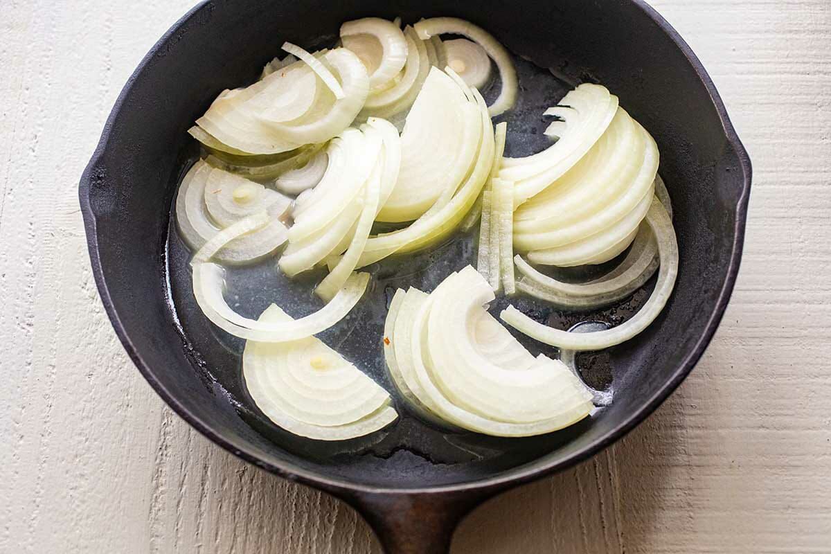 A cast iron skillet with sliced onions to show how to make a patty melt.