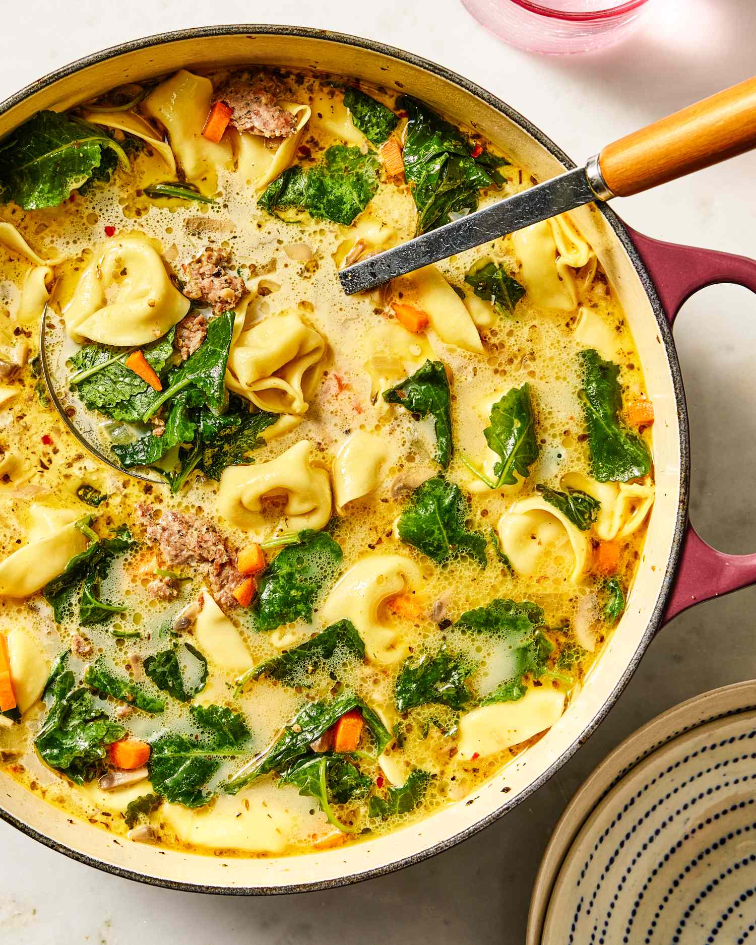 A pot of creamy tortellini soup with spinach and vegetables
