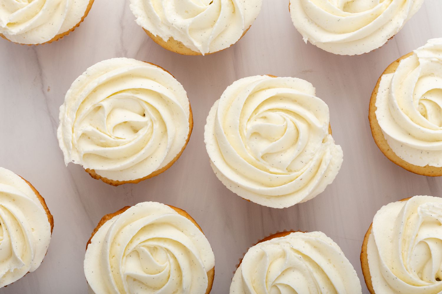Overhead view of vanilla cupcakes with vanilla frosting set on a light colored background.