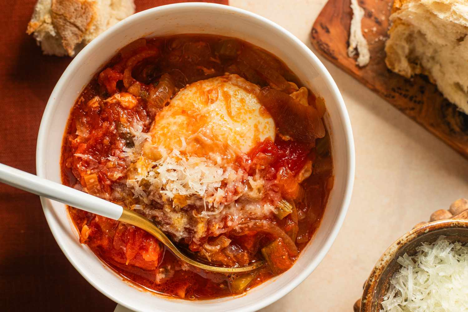 Overhead view of Acquacotta (Tuscan Soup) in a white bowl with a spoon plus bread on a cutting board and Pecorino romano cheese in a bowl to the side