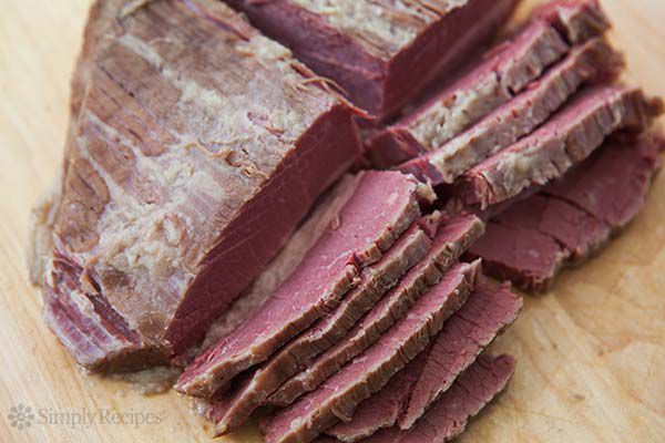 Fully cooked corned beef being sliced on a cutting board