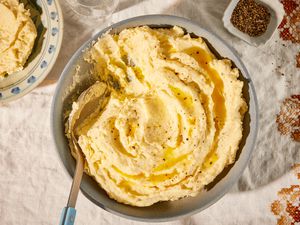 Overhead view of a gray bowl of almond milk mashed potatoes with a spoon and topped with butter on top of a fall themed embroidered cloth