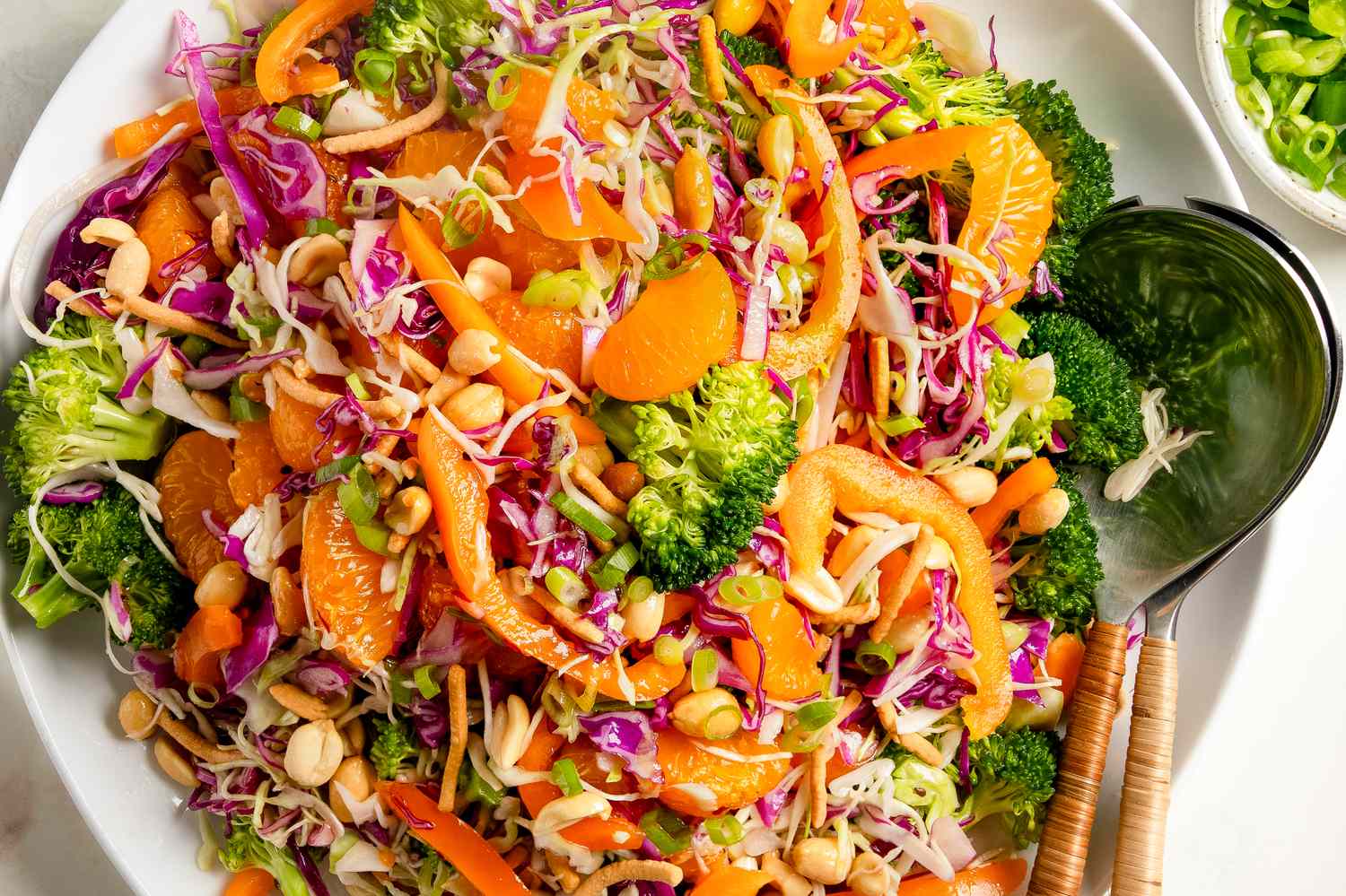 A bowl of broccoli crunch salad with mandarin oranges peanuts shredded vegetables and a spoon