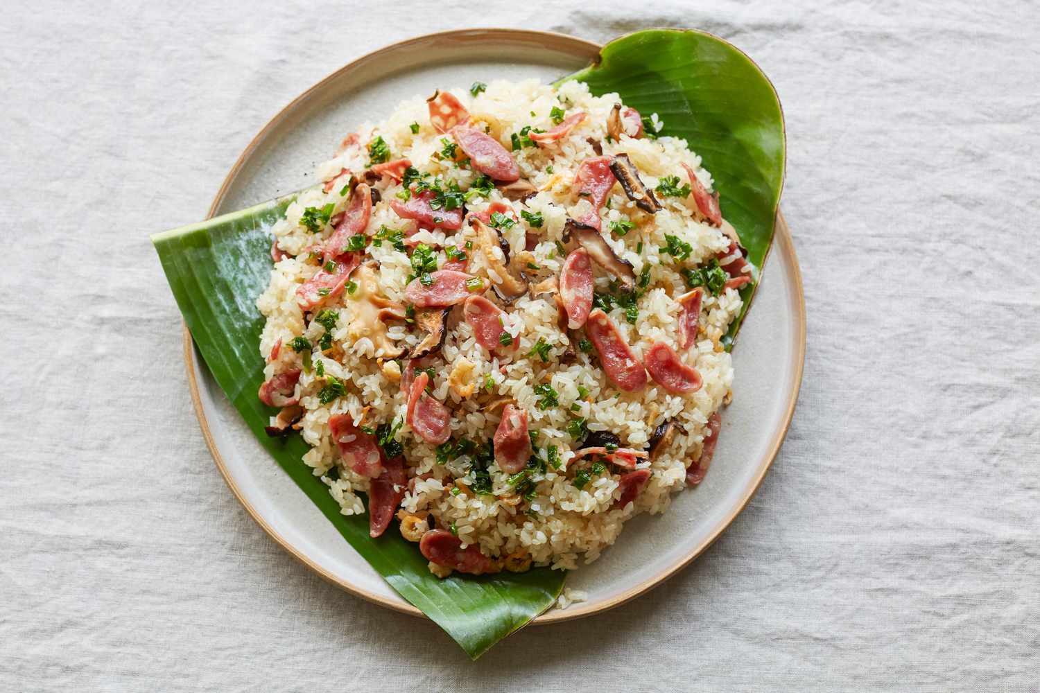 Steamed rice with sausage, dried shrimp, and mushrooms served on top of banana leaves.