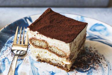 A slice of tiramisu on a plate with the pan of tiramisu in the background