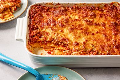 Side view of a white baking dish of Million Dollar Ravioli Casserole with a serving removed and on a small plate next to a serving spoon on a small plate