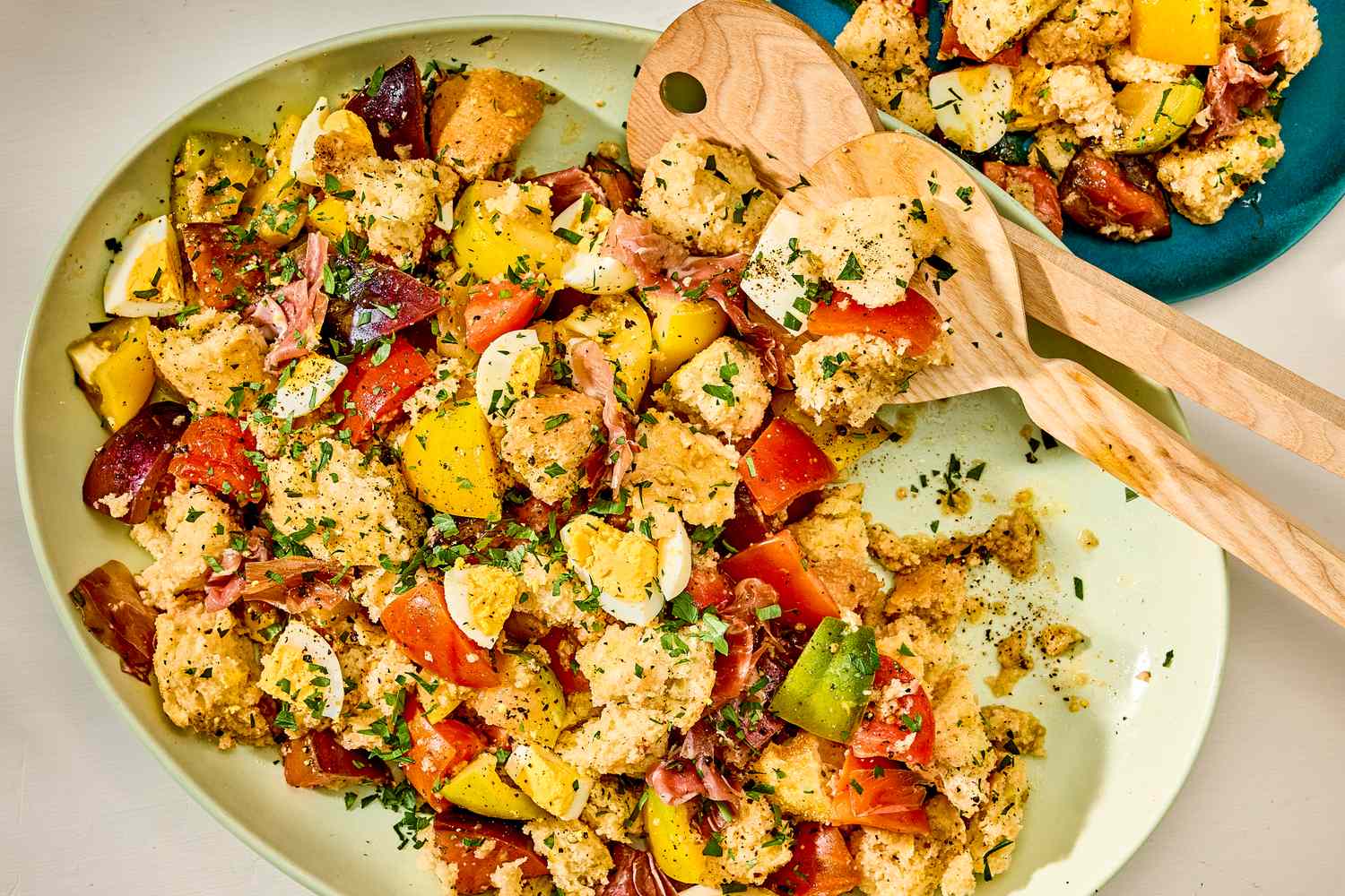 Platter with a salad of bread cubes, tomatoes, zucchini, and herbs, wooden serving utensils on the plate
