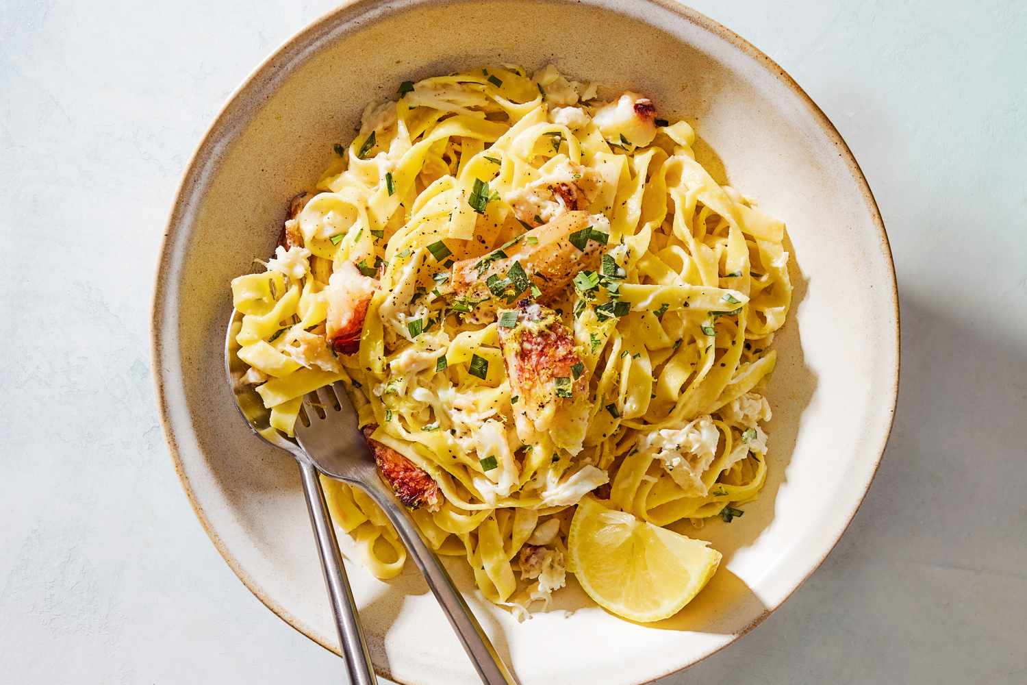 Overhead shot of a bowl with a 5-ingredient creamy crab pasta, with a lemon wedge and chopped fresh tarragon as garnish