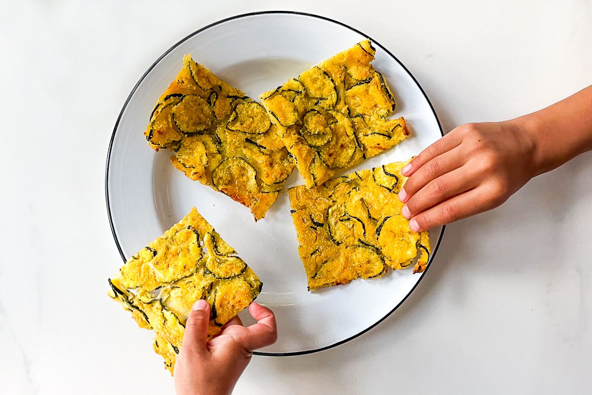 two hands taking pieces of Tuscan zucchini scarpaccia from a plate