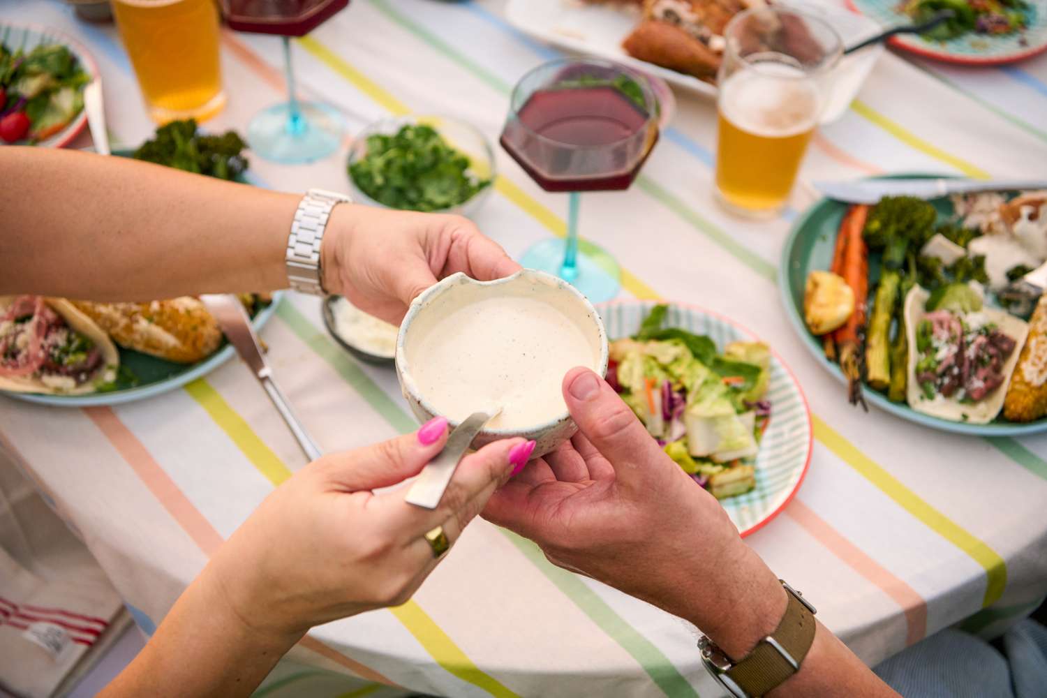 Two people at a table with a bowl of sauce, food and drinks served on plates visible in the background