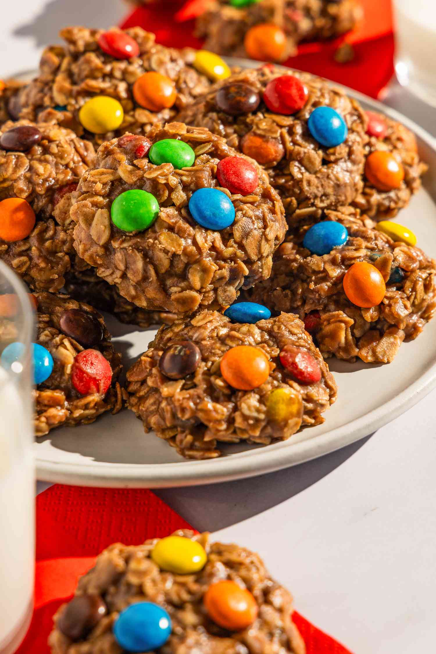 Plate of no-bake m&m cookies next to a glass of milk and more cookies on the counter on napkins