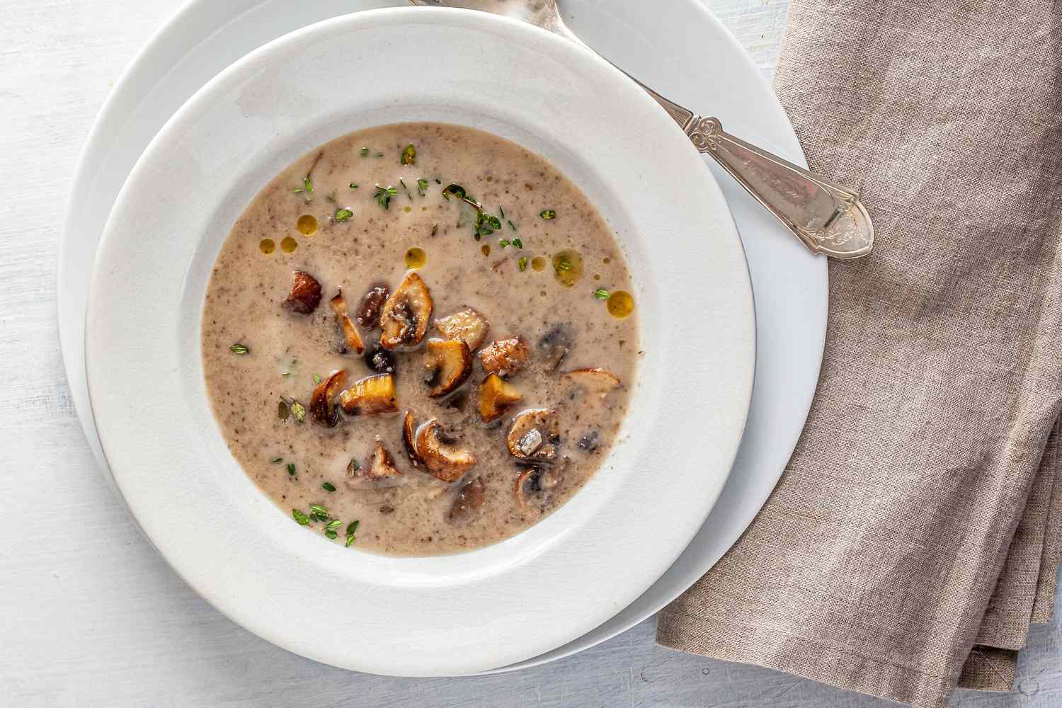 Chestnut mushroom soup in a white bowl with a white plate underneath.