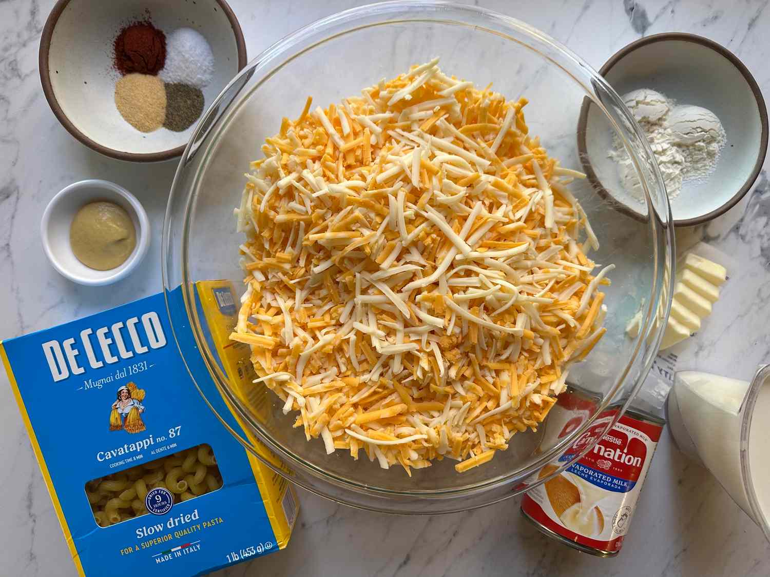 Ingredients for making macaroni and cheese including shredded cheese pasta evaporated milk flour and spices