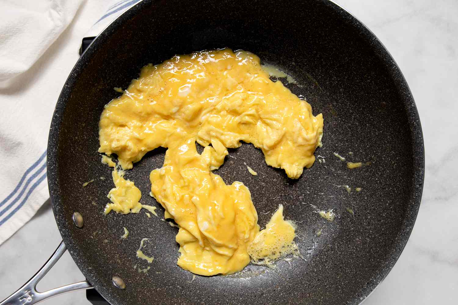 Overhead of a hand holding a spatula scrambling eggs in a pan