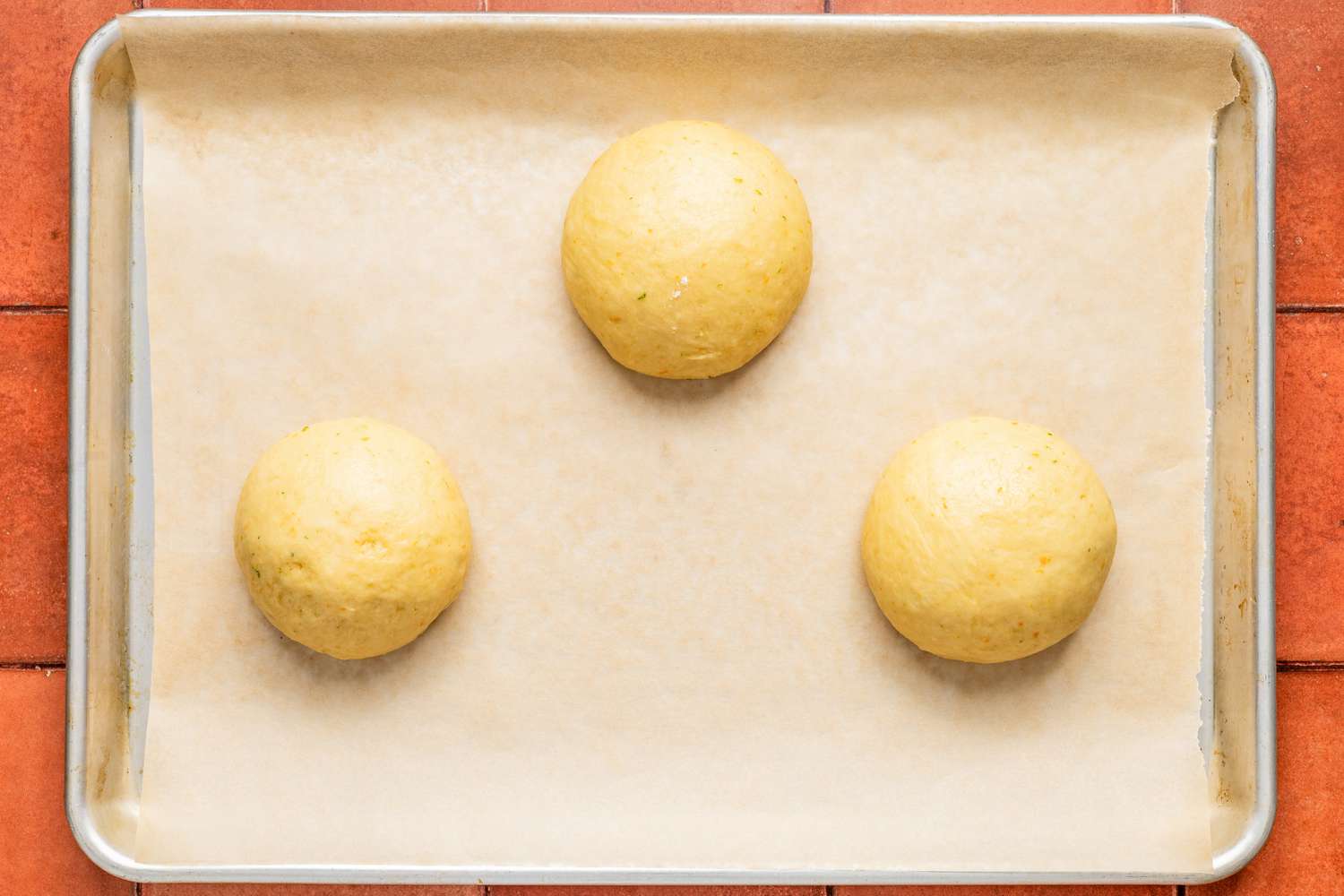 Three dough balls on a parchment paper lined baking sheet for pan de muerto recipe
