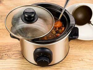 Slow cooker with stew ladle and plate on wooden table