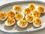 A ceramic serving plate with million dollar deviled eggs, garnished with chopped chives and paprika