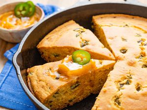 Hot honey cornbread (JalapeÃ±o Honey Cornbread) sliced in a cast iron skillet with one slice topped with hot honey butter