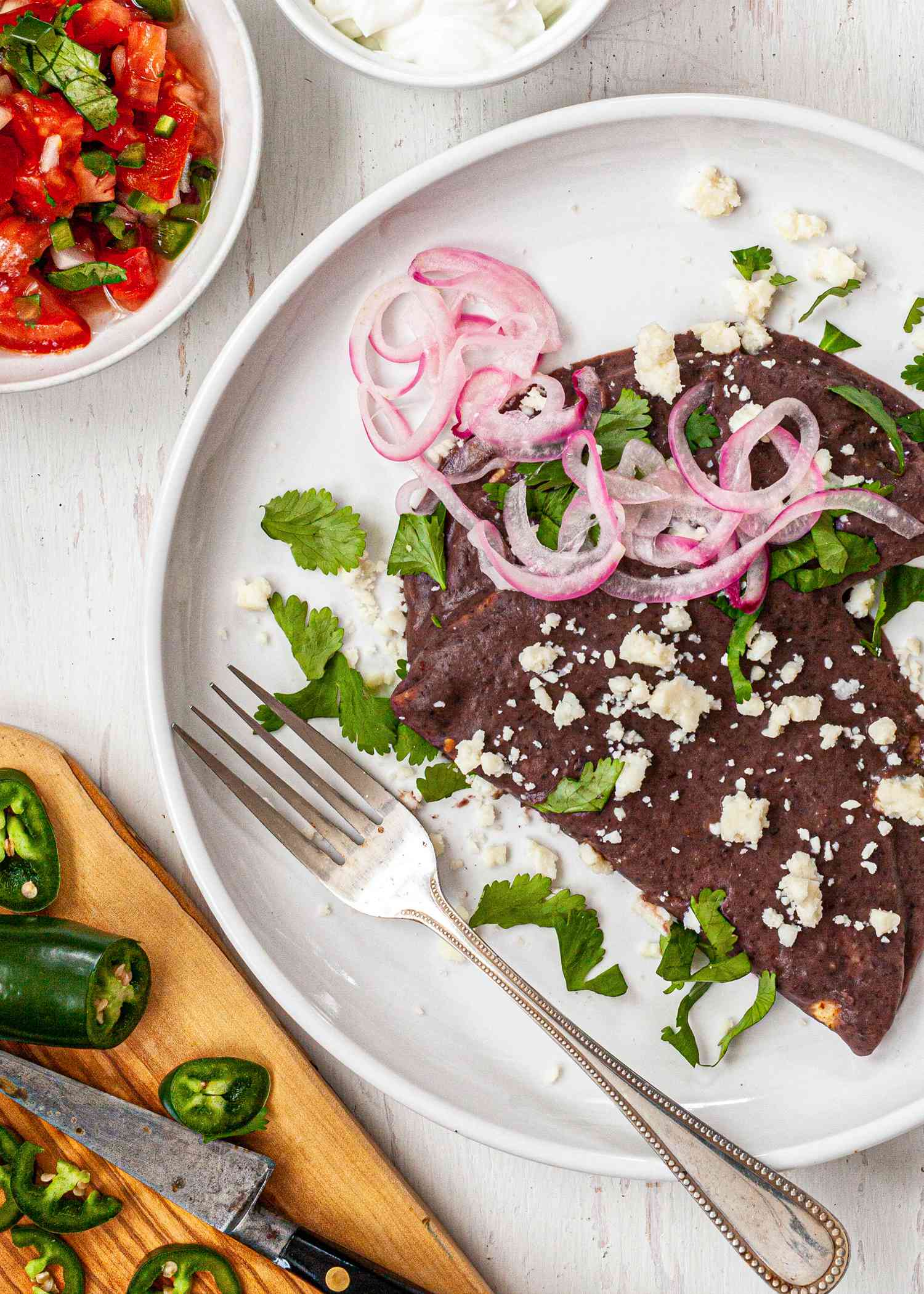 Black Bean Enfrijoladas topped with red onions and cojita.