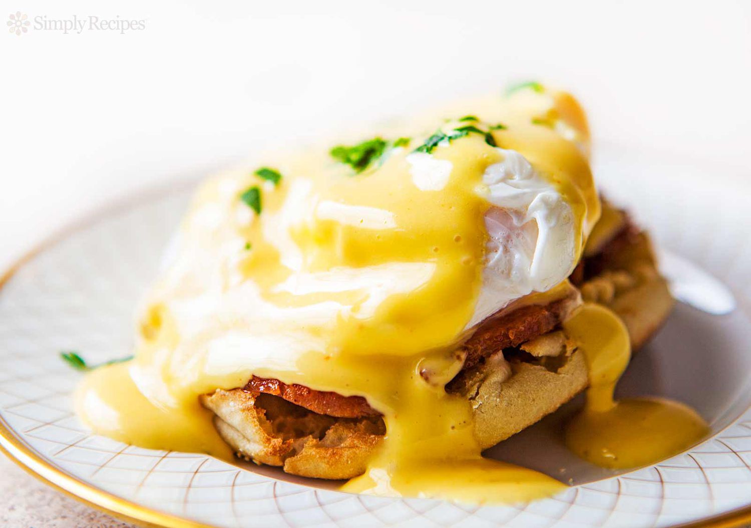 Eggs Benedict resting on a white and gold plate