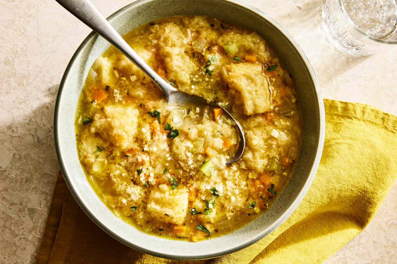 A bowl of pancotto with a spoon accompanied by a yellow napkin