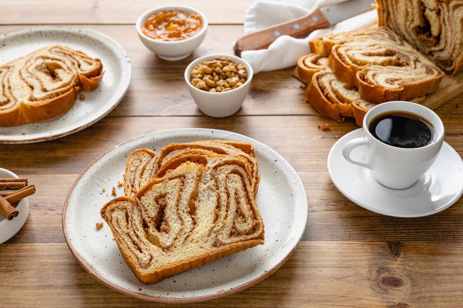 Plates with Slices of Povitica Surrounded by a Cutting Board with More Slices, Small Bowls of Ingredients (Pecans, Cinnamon, etc), and a Cup of Coffee