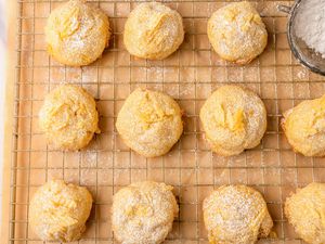 Overhead view of potato chip cookies on a cooling rack over parchment paper next to a owl of powdered sugar
