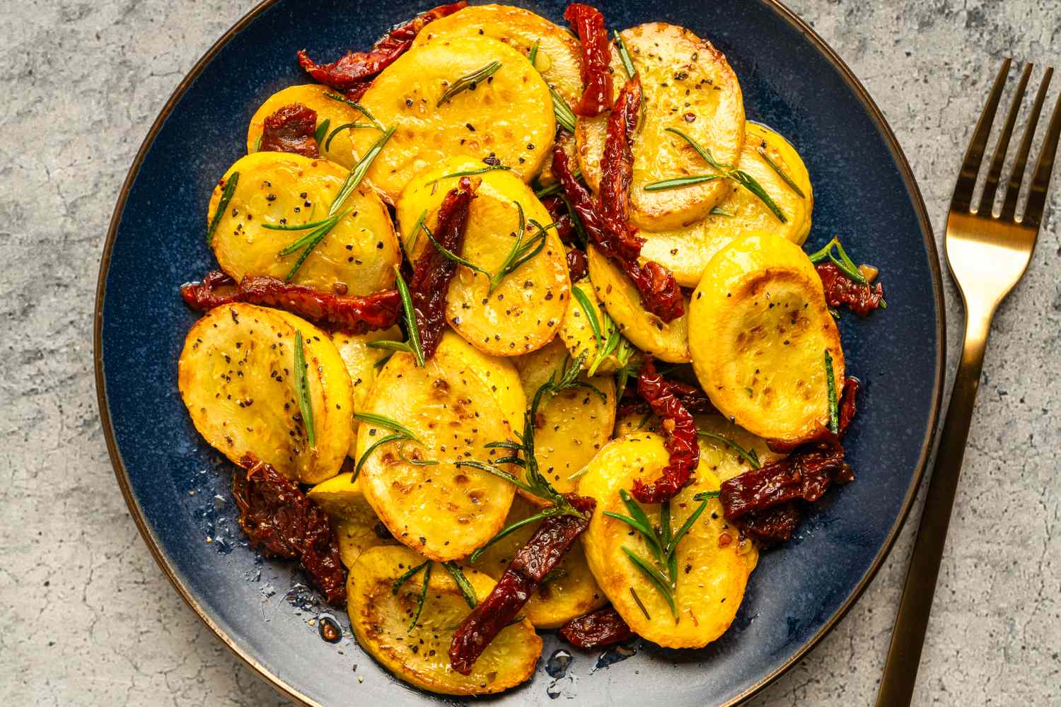 A plate of zucchini pieces garnished with herbs and sundried tomatoes arranged on a blue plate with a fork placed to the side