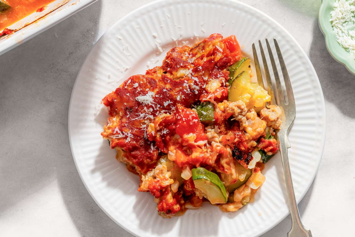 A plate of zucchini pizza bake served with a fork showcasing melted cheese and vegetables in a tomatobased sauce