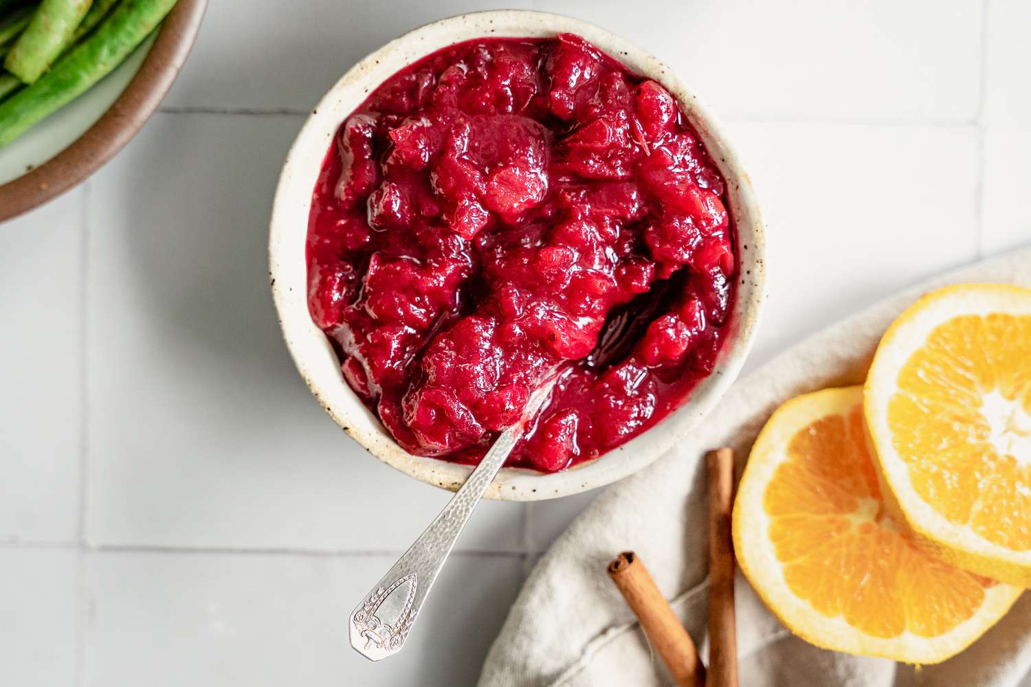 Instant Pot Cranberry Sauce Next to a Bowl of Green Beans and Table Napkin with Orange Slices and Cinnamon Sticks