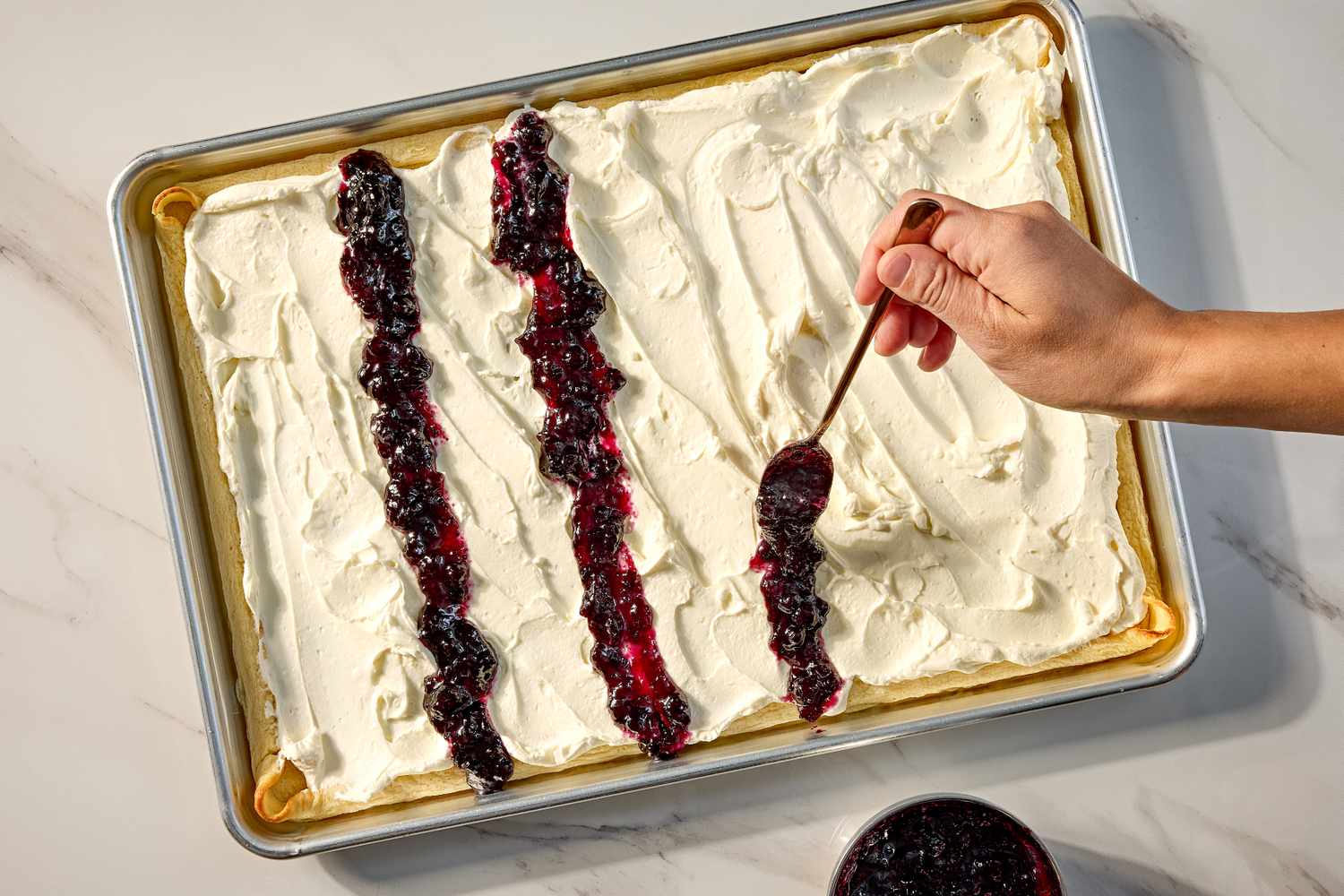 A hand spreading berry compote over a cream covered crepe cake in a baking sheet for the lazy crêpe cake recipe