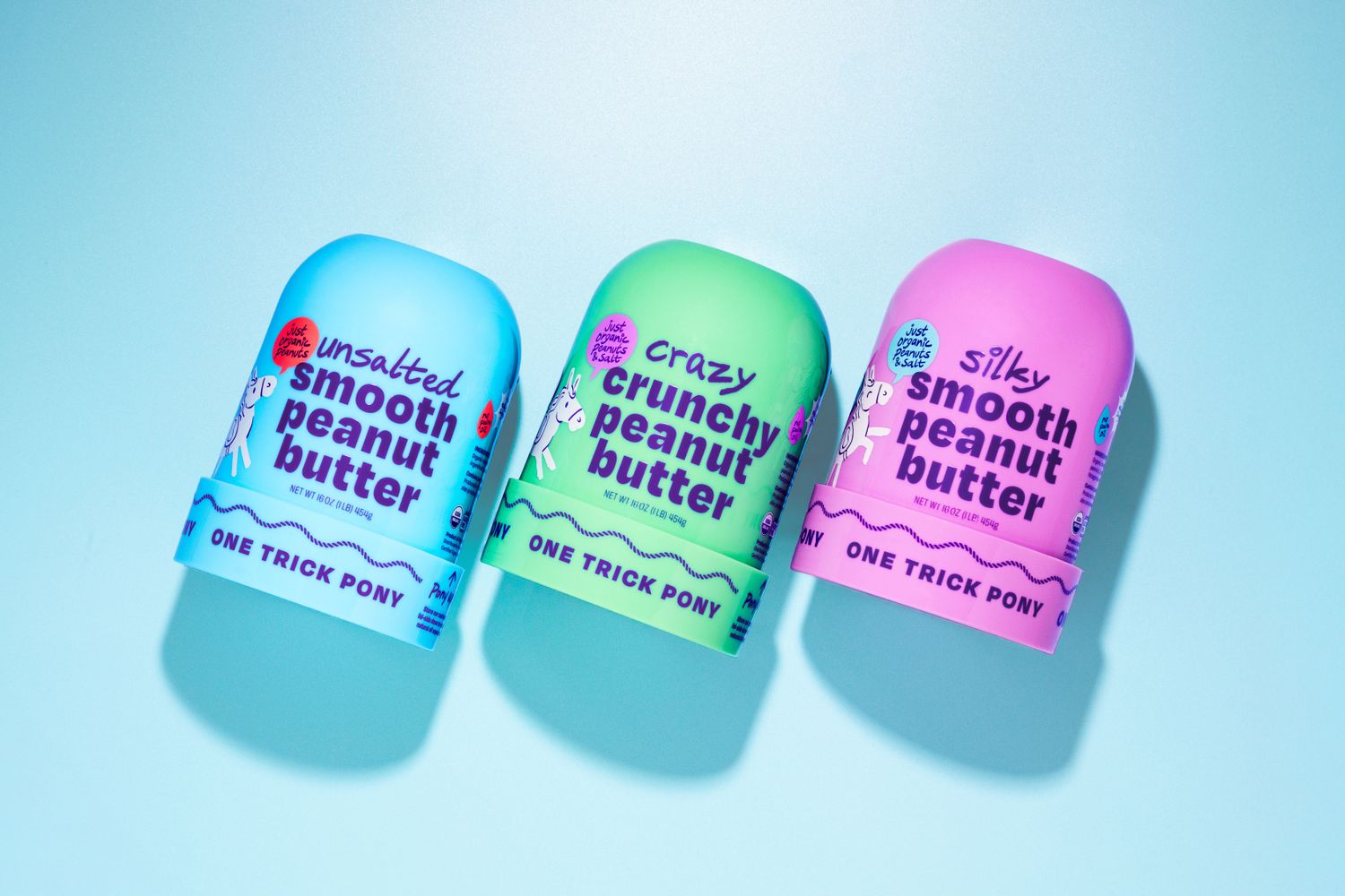 Three jars labeled as smooth crunchy and silky peanut butter from One Trick Pony on a light background