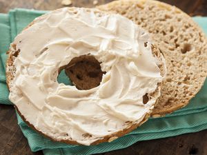 A bagel half spread with cream cheese on a turquoise fabric surface