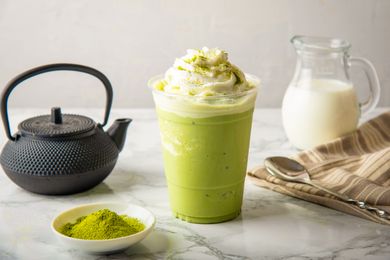 Iced matcha latte topped with whipped cream teapot and matcha powder in the background