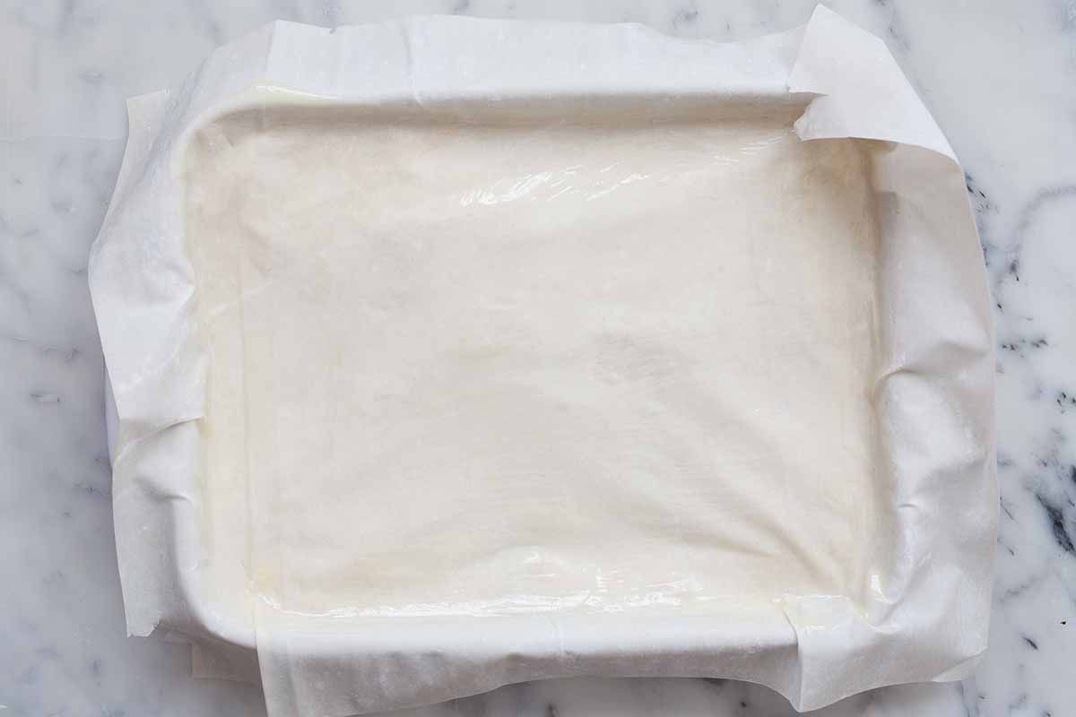 Phyllo covering the top of of a casserole dish filled with spinach and cheese for spanakopita.