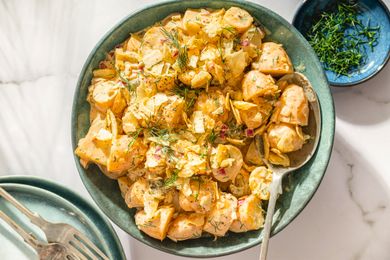 A bowl of dill pickle potato salad with a serving spoon