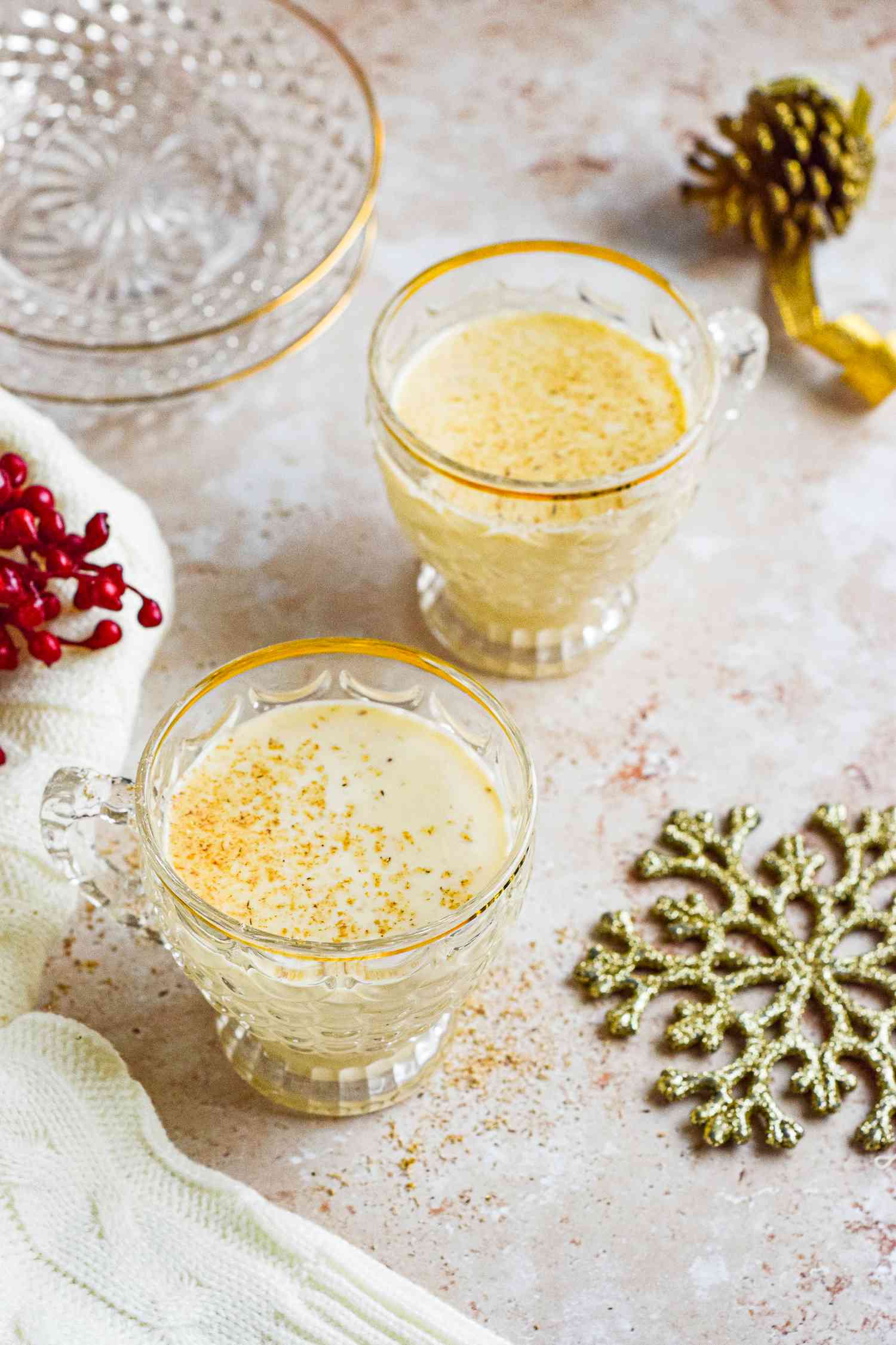 Two gold-rimmed glasses of eggnog cocktail.