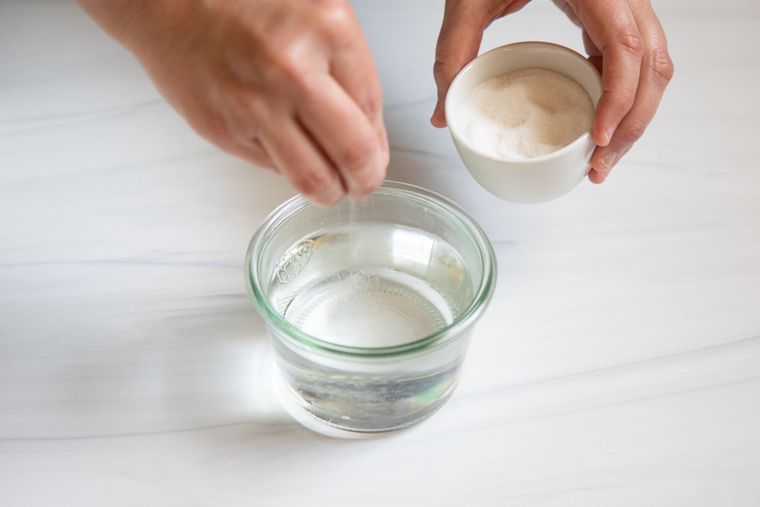 A small glass cup of water with dry yeast being added to it.