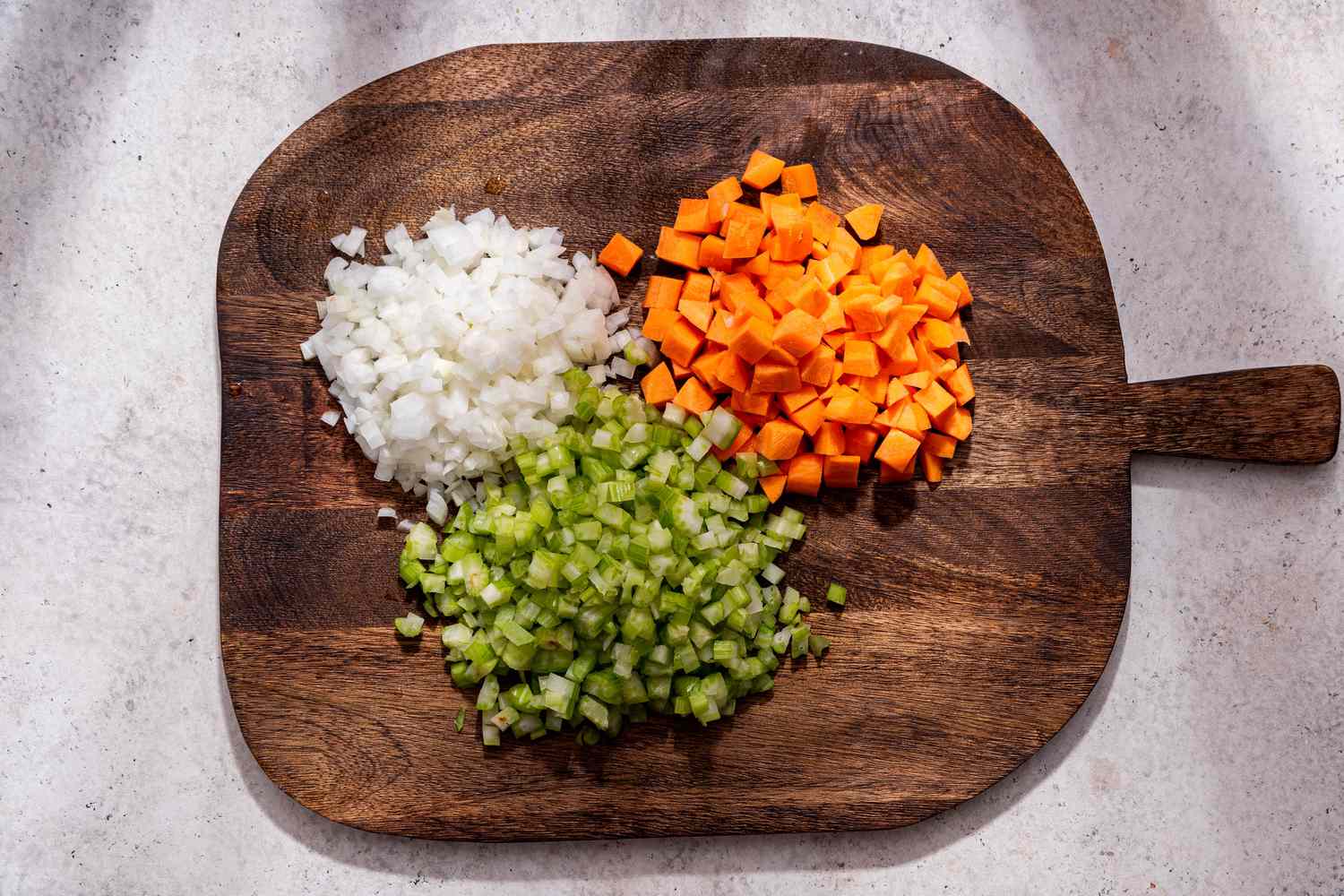 Chopped stock vegetables (onions, carrots, and celery) on a wooden board 