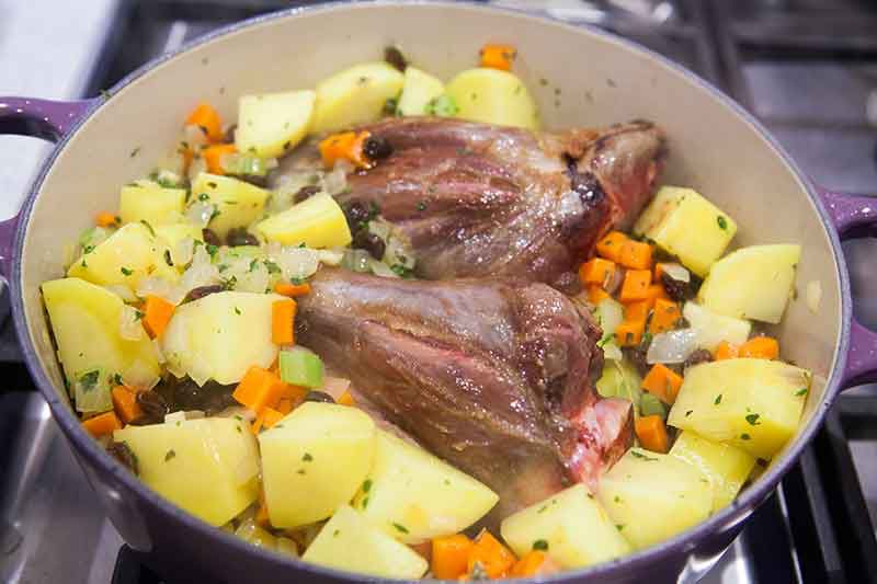 Lamb shank cooking with potatoes, carrots onion and celery in oven proof pan