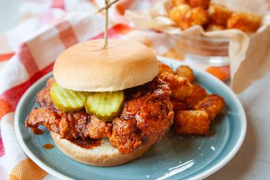Nashville hot chicken sandwich with pickles and served on a plate.