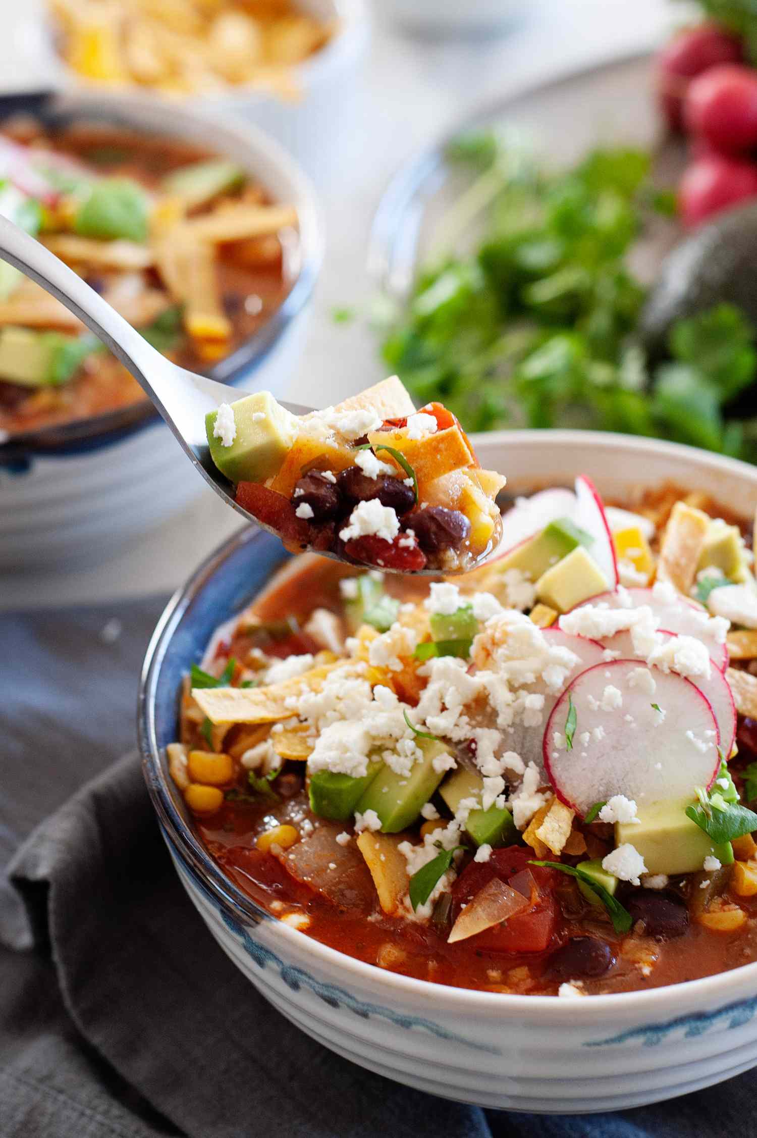 Vegetarian-friendly tortilla soup in a bowl and topped with sour cream, avocado, and tortilla strips.