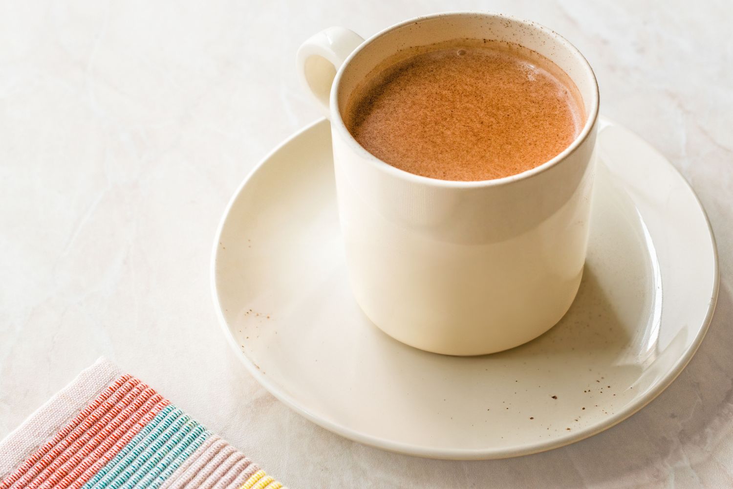 A cup of hot cocoa on a saucer next to a colorful napkin