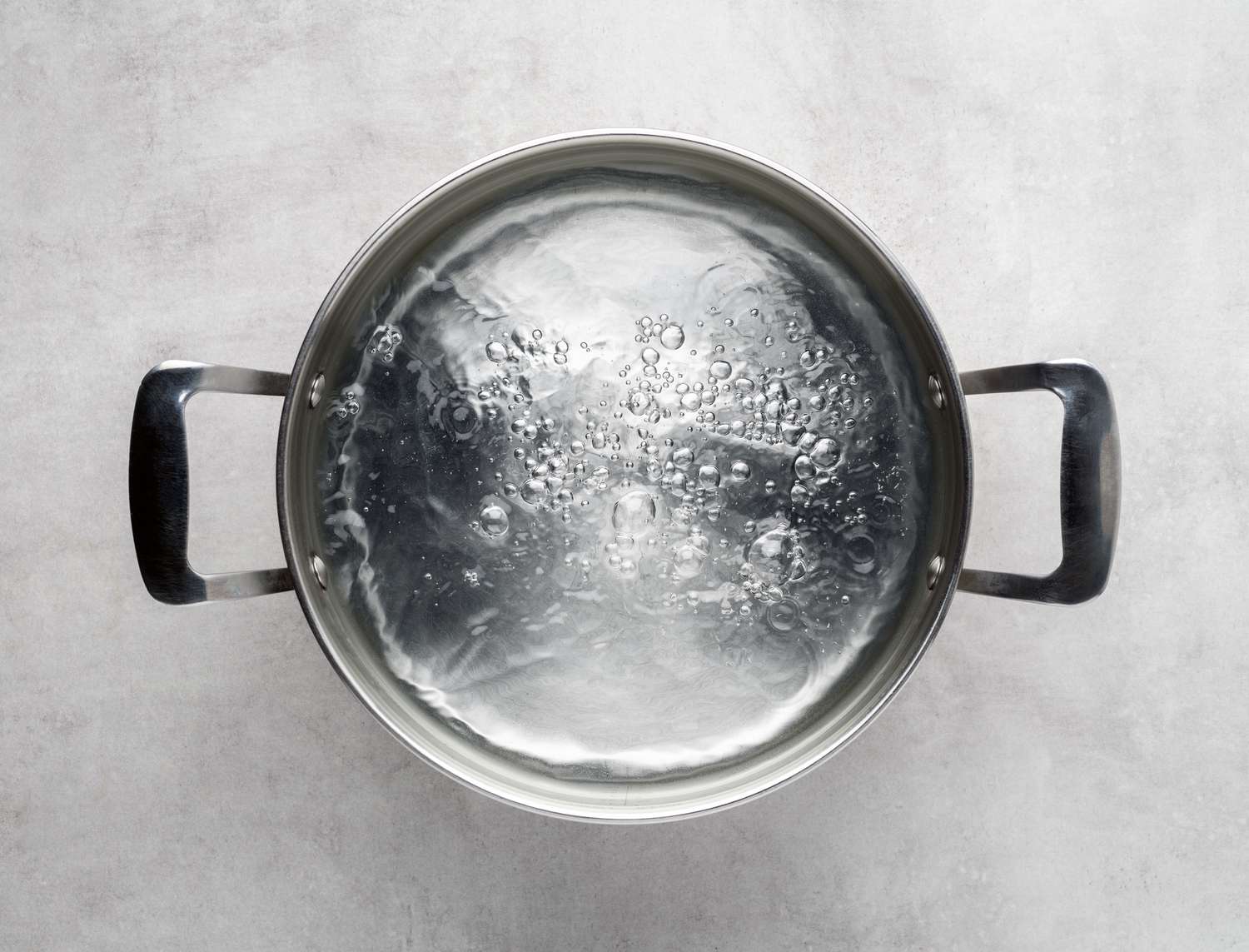 Overhead shot of a stainless steel metal cooking pot of boiling water on gray concrete background