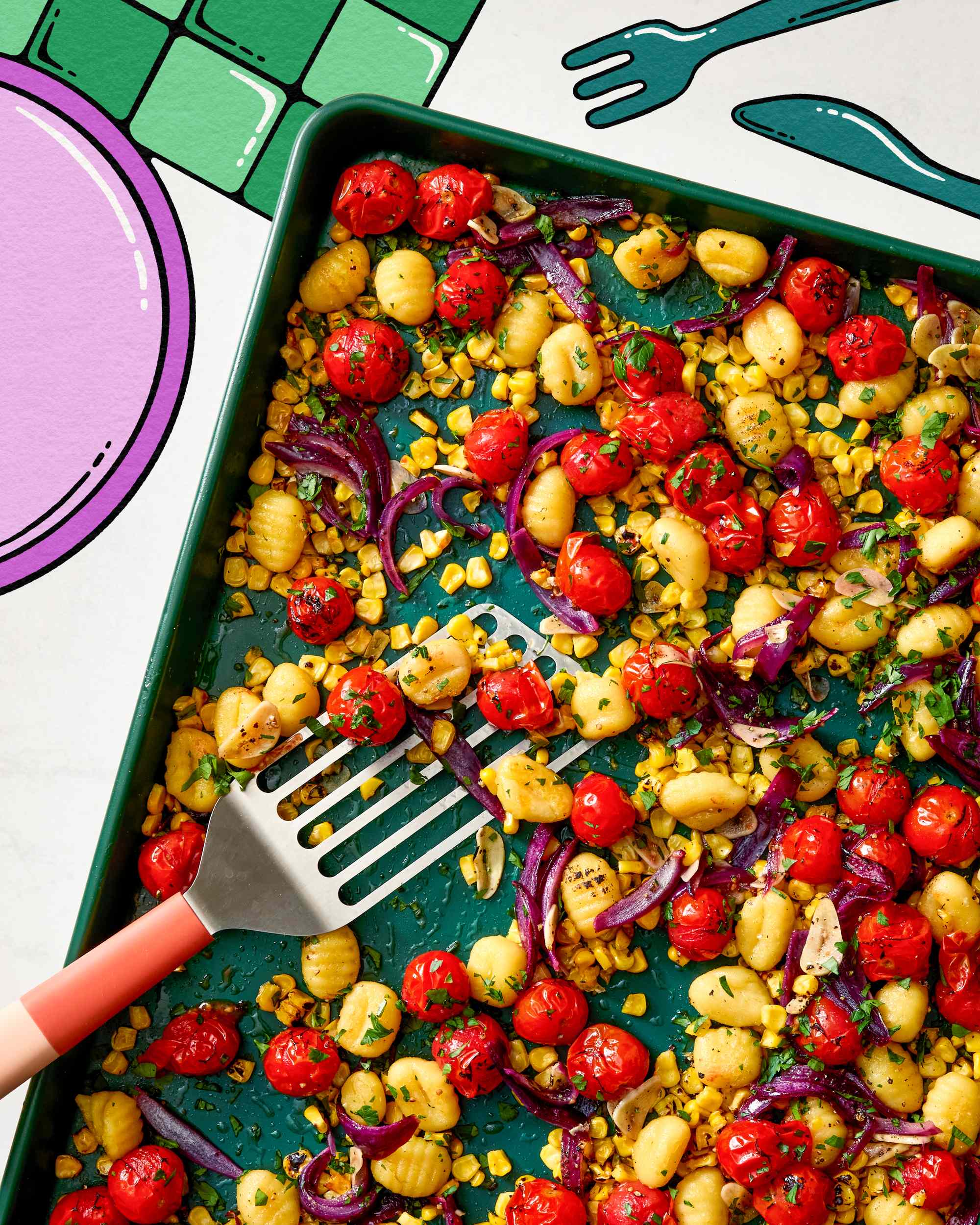 A tray of roasted gnocchi cherry tomatoes corn and red onions with a spatula