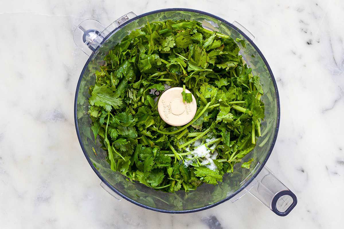 Food processor set on a marble background with cilantro and salt visible inside.