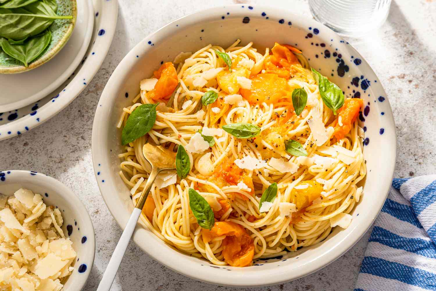 fresh tomato pasta in a bowl next to a bowl of shaved parmesan and small plate with basil