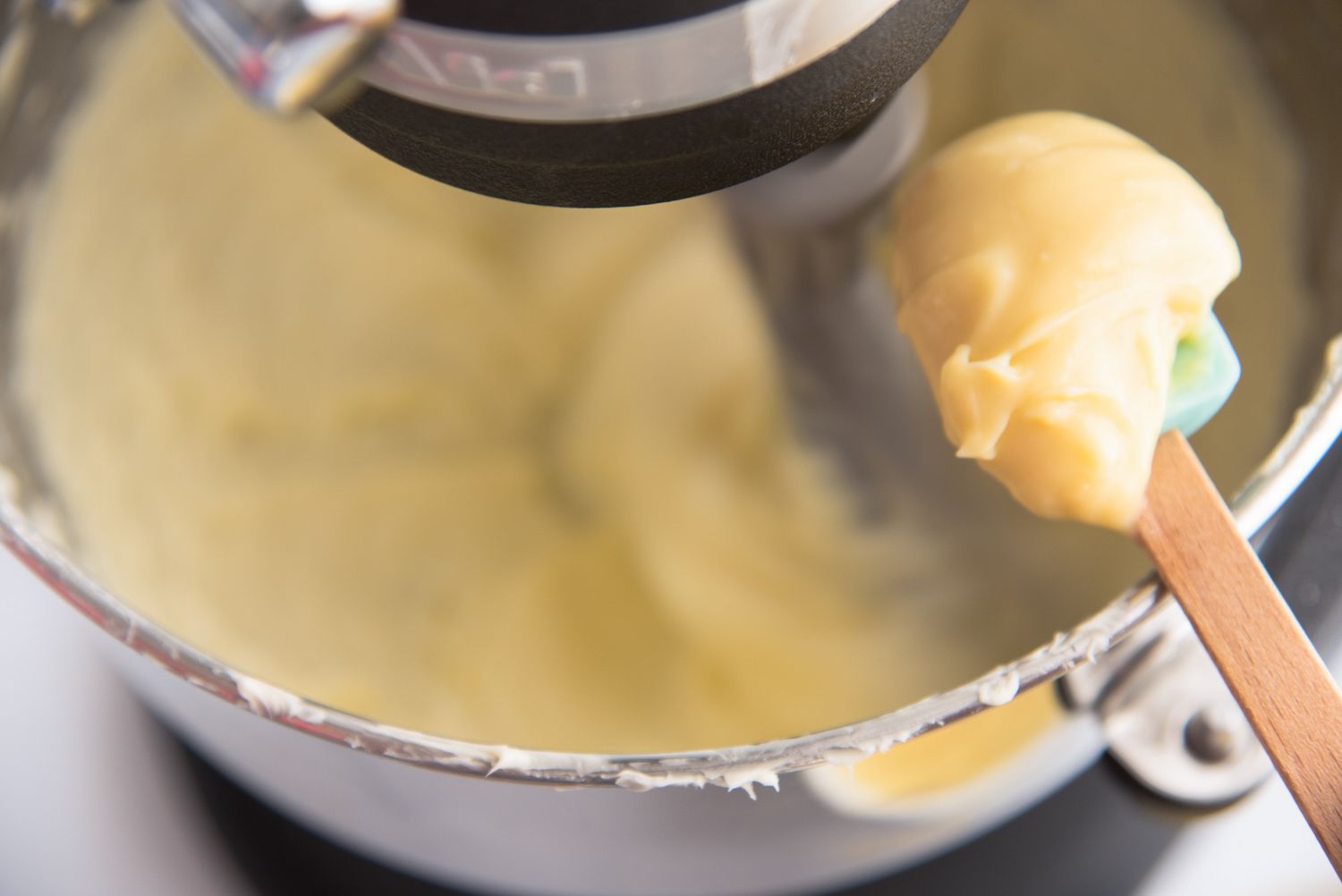 A spatula with creamy German buttercream held above a mixer bowl of more frosting.