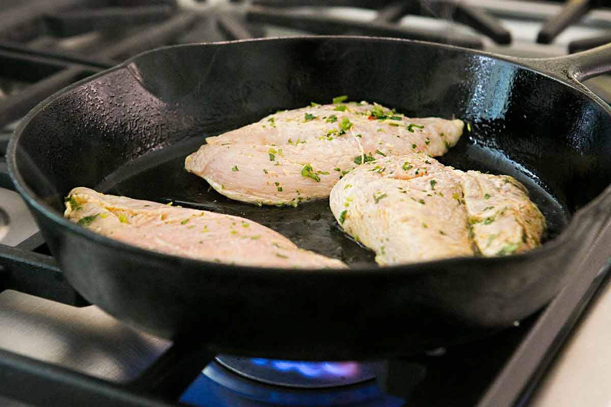 Three pieces of chicken cooking in a cast iron skillet